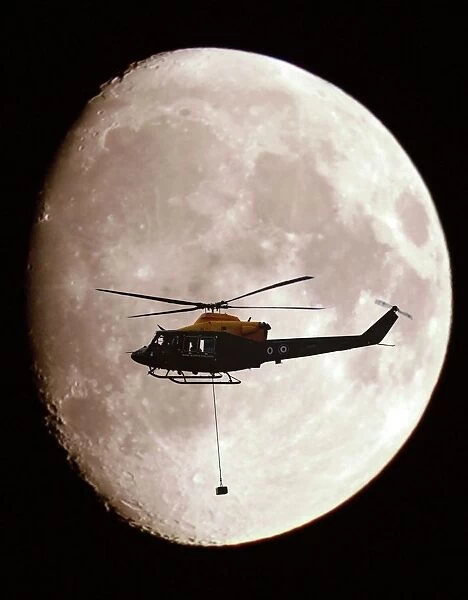 A Griffin Helicopter, with an underslung load, shown in silhouette against a full moon