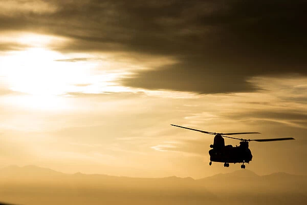 An RAF Chinook helicopter in silhouette, flying over Afghanistan