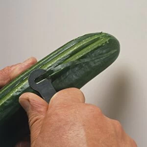 Person peeling cucumber with peeler, close-up