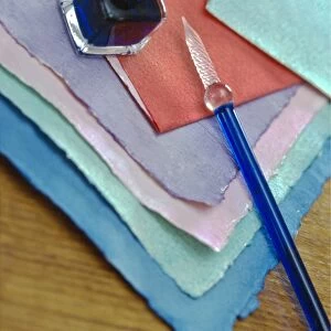 Selection of pastel coloured handmade papers with glass pen and small bottle of ink